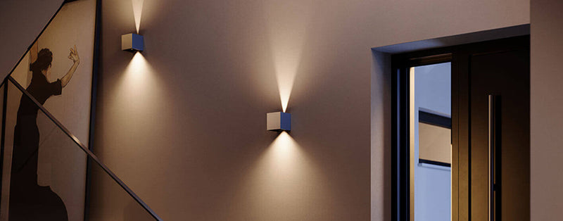 Moderne Wandleuchten beleuchten einen eleganten Flur mit Kunstwerk und Eingangstür.