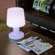 LED-Akku-Tischleuchte Carmen 45cm mit Fernbedienung auf einem Tisch neben einem Magazin.