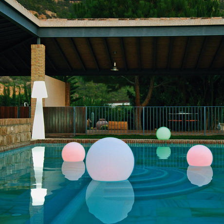 Une piscine avec la sphère lumineuse Buly Ø 60cm LED et d'autres lampes sphériques flottantes à la lumière du crépuscule.