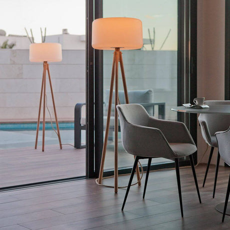 Candeeiro de pé tripé LED Chloe com bateria e comando à distância num espaço de estar moderno com cadeiras e vista para a piscina.