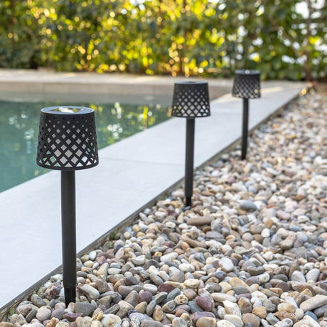 Set de 4 piquets solaires LED Gretita IP44 fixé à côté d'une piscine sur gravier, idéal pour l'éclairage de jardin.