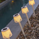 Gretita LED Garten-Solarspieß IP44 im Garten bei Nacht, stilvolles Licht neben Steinen am Wasser.