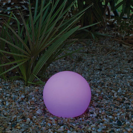 Boule lumineuse Buly Ø 20 cm éclaire en rose doux dans le jardin sur un sol en gravier.