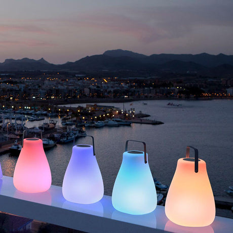Draagbare LED-luidsprekerlamp Kurby Wit op een balkon met zeezicht bij zonsondergang.