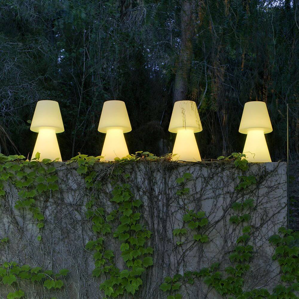 Lola LED-Außen-Tischleuchte Large in einem Garten mit Pflanzen, sanft leuchtend und elegant im Design.