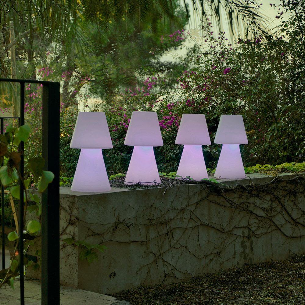 Lola LED-Außen-Tischleuchte Large in einem Garten mit verschiedenen Beleuchtungen und Pflanzen.