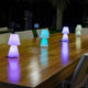 Lola LED-Außen-Tischleuchte Small auf einem Holztisch, ideal für Garten und Terrasse, in verschiedenen Farbvariationen.