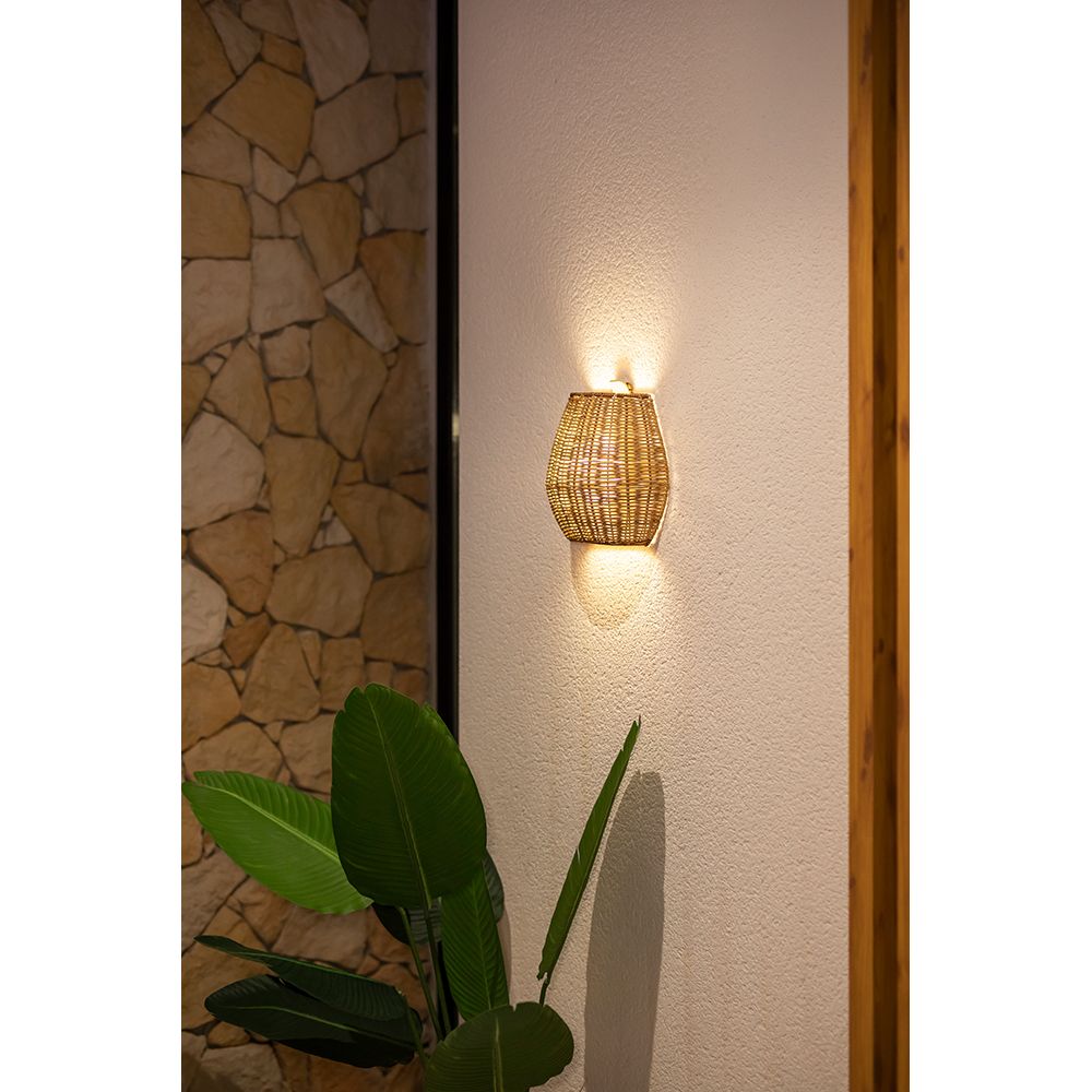 Saona Boho-Style Wand-Akkuleuchte aus Rattan, dimmbar und fernbedienbar, an einer Wand mit Pflanzen.