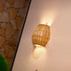 Saona Boho-Style LED Wand-Akkuleuchte aus Rattan IP54 an einer Wand montiert, mit warmem Licht.