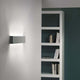 Box W2 LED-Wandleuchte Medium Warmweiß an einer Wand, moderne Einrichtung mit Bücherregal im Hintergrund.