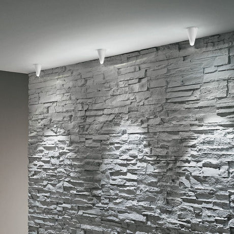 Conus X LED-Deckenleuchte an einer modernen Steinwand, dekorative Beleuchtung im Innenbereich.