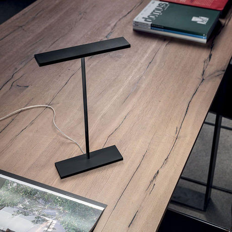 Dublight C tab LED-Tischleuchte auf einem schlichten Holztisch, umgeben von Büchern und Zeitschriften.