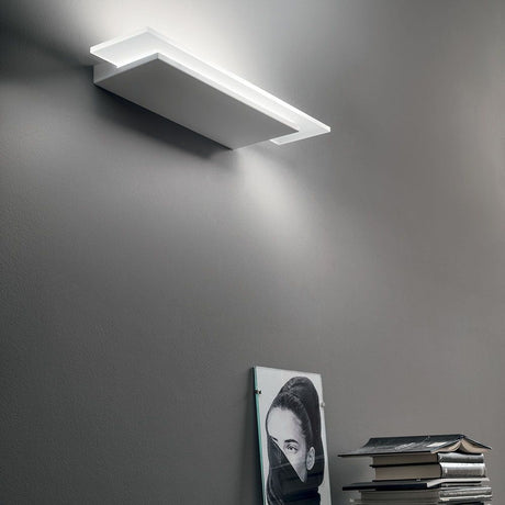 Dublight W LED-Wandleuchte an einer Wand mit Bücherstapel und einem Kunstwerk.