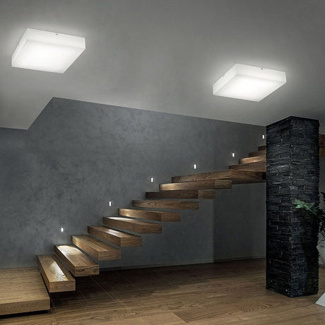 Plafonnier Gluèd SQ LED dans une cage d’escalier moderne avec des marches en bois et des accents lumineux élégants.