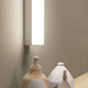 Kioo LED-Wandleuchte Big an Wand, mit dekorativen Vasen im Vordergrund auf einem Tisch.