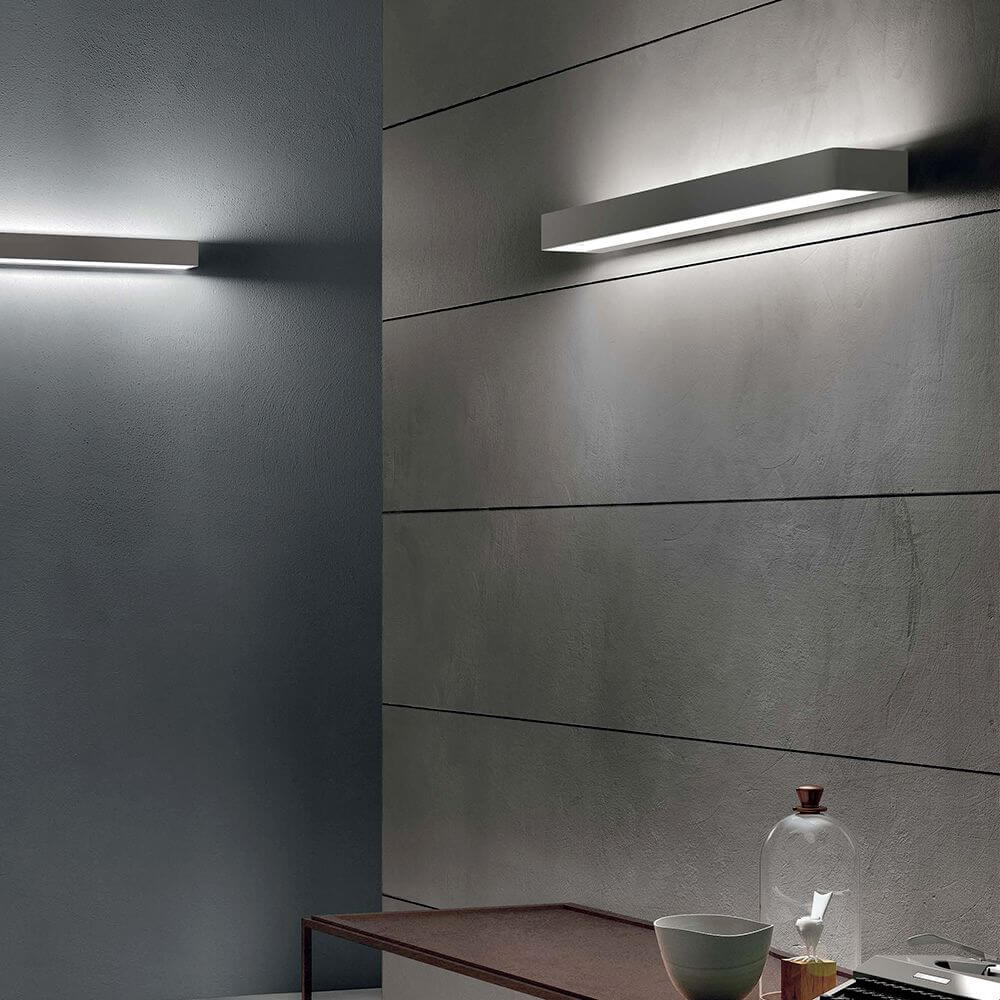 Moderne Einrichtung mit Metal W LED-Wandleuchte Large an der Wand und stilvollem Tisch mit Dekoration.