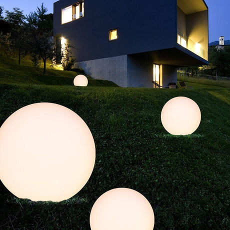 Oh! FL65 LED-Bodenleuchte im Garten mit leuchtenden, runden Lampen vor modernem Gebäude.