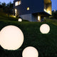 Oh! FL65 LED-Bodenleuchte im Garten mit leuchtenden, runden Lampen vor modernem Gebäude.