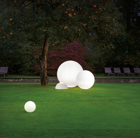 Oh! FL65 decorative light shines softly in the garden, surrounded by trees and lawn.
