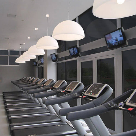 Modern gym with Ohps P pendant light above treadmills and televisions on the wall.