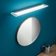 Skinny LED-Wandleuchte Small über runder Spiegelfläche an blauer Wand.