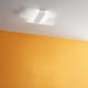 Triad 2.0 LED-Deckenleuchte an einer Decke mit orangefarbener Wand im Hintergrund.