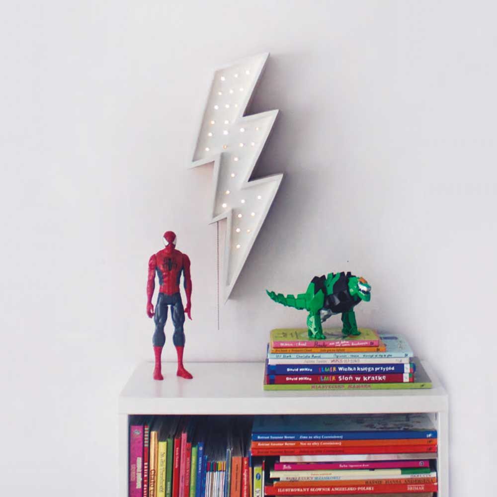 Holzlampe in Blitzform mit dimmbarer Lichtintensität, neben Superheldenfiguren und bunten Kinderbüchern.