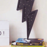 Holzlampe in Blitzform mit Dimmer, auf einem Bücherstapel platziert, ideal für Kinderzimmer.