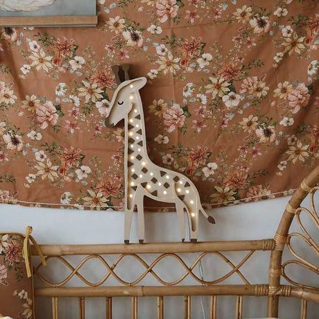 Kinder Wand- & Tischleuchte Giraffe auf einem Bett mit floraler Decke.