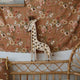 Kinder Wand- & Tischleuchte Giraffe auf einem Bett mit floraler Decke.