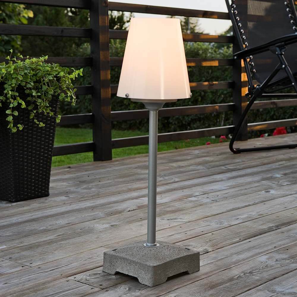 Lucca Terrassenleuchte klein mit massiven Betonfuß Grau auf Holzterrasse, modernes Design mit diffusionsfilterndem Lampenschirm.