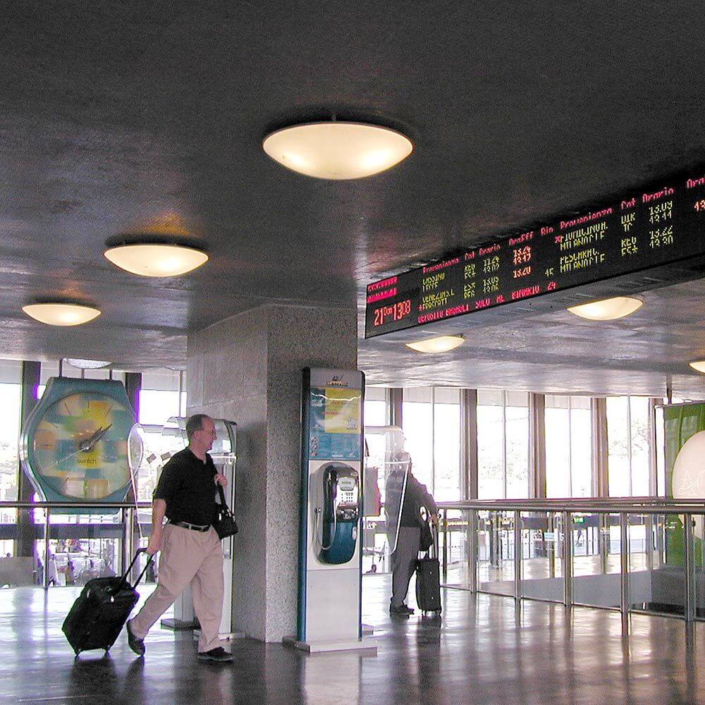 Helle Luceplan Deckenleuchte Trama im Empfangsbereich eines Bahnhofs mit digitalen Anzeigetafeln.