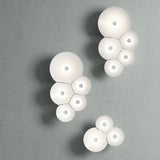 Luceplan Bulbullia Wandleuchte mit organischem Design in Weiß, inspiriert von Seifenblasen, an grauer Wand.
