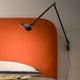 Luceplan Otto Watt Wandhalterung an einer orangefarbenen Wand über einem Bett.