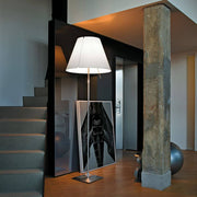 Luceplan Stehlampe Grande Costanza mit Sensor-Dimmer in modernem Raum, neben einer Treppe und Kunstwerk.