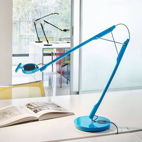 Luceplan Tivedo LED Büro-Tischleuchte 3000K in blauer Farbe auf einem Schreibtisch mit einem offenen Buch.