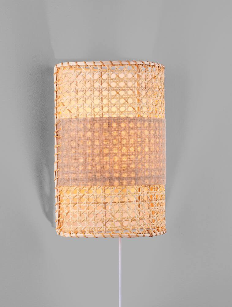 Lum Wandleuchte Natur aus Rattan mit warmem Licht an einer grauen Wand