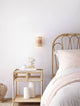 Lum Wandleuchte Natur mit Rattan-Design neben einem Bett in einem hellen Schlafzimmer.