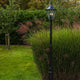 Lutec London Außen-Standleuchte IP44 300lm in einem Garten, umgeben von hohem Gras.