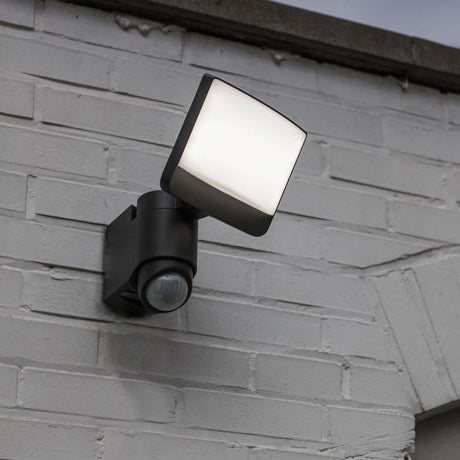 Lutec Sunshine LED-applique murale d’extérieur IP44 500 lm noir disposée sur un mur blanc avec détecteur de mouvement.