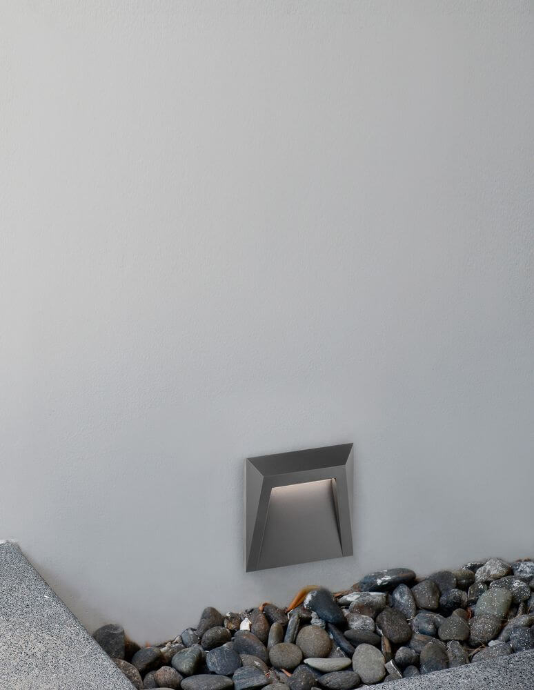Luton LED Außenwandleuchte Lichtauslass Kegel 3000K Dunkelgrau IP65 an Wand mit Steinen.