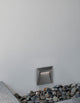 Luton LED Außenwandleuchte Lichtauslass Kegel 3000K Dunkelgrau IP65 an Wand mit Steinen.