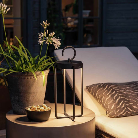 Lanterne d’extérieur CCT Manorola LED sur une table avec une plante et un bol à snacks dans un espace extérieur chaleureux.