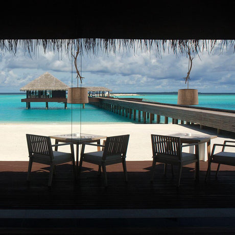 View of a relaxing beach with terrace tables and a wooden jetty in the background.