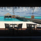 Blick auf einen entspannenden Strand mit Terrassentischen und Holzanlegestelle im Hintergrund.
