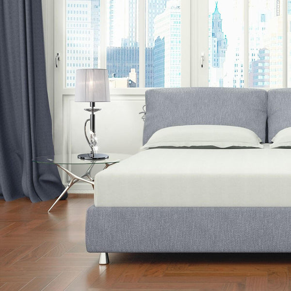 Vue moderne d’une chambre avec lampe de table Tiffany, lit et table d’appoint en verre.