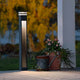 Massa LED Wegeleuchte Anthrazit, klares Acrylglas mit dekorativen Pflanzen und Gießkanne im Garten.