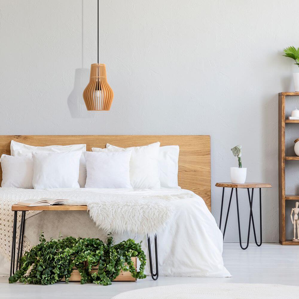 Holz Hängeleuchte Roots in Tropfenform über einem Bett mit weißen Kissen und Holzregal im Hintergrund.