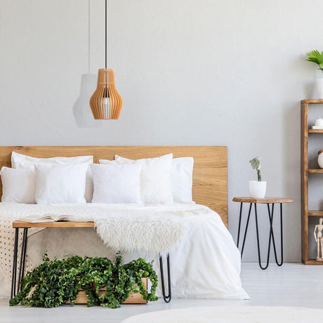 Holz Hängeleuchte Roots in Tropfenform über einem Bett mit weißen Kissen und Holzregal im Hintergrund.