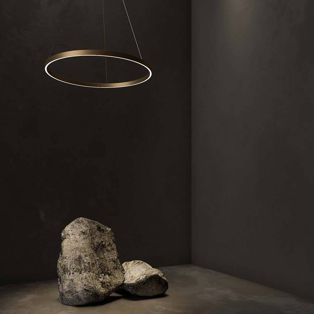 Rim LED Ring Pendellampe in Messing, modernes Design in einem minimalistischen Raum mit Steinen.